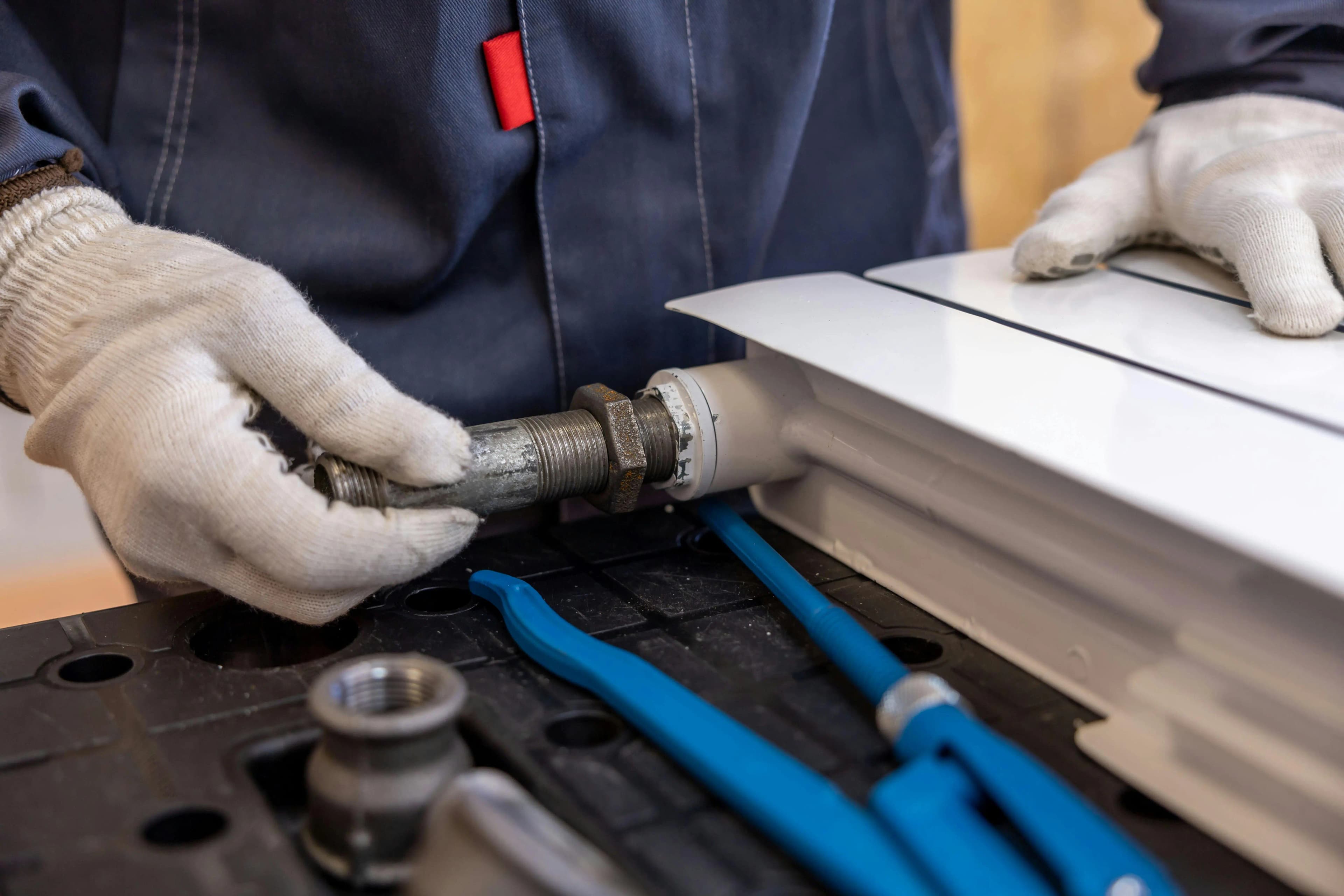 Gloved hands holding a pipework connection at a white radiator during plumbing work.